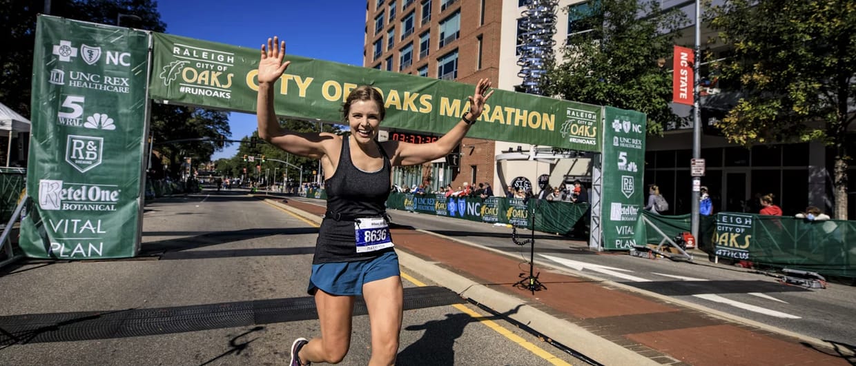 A runner crossing a marathon finish line, arms raised and smiling