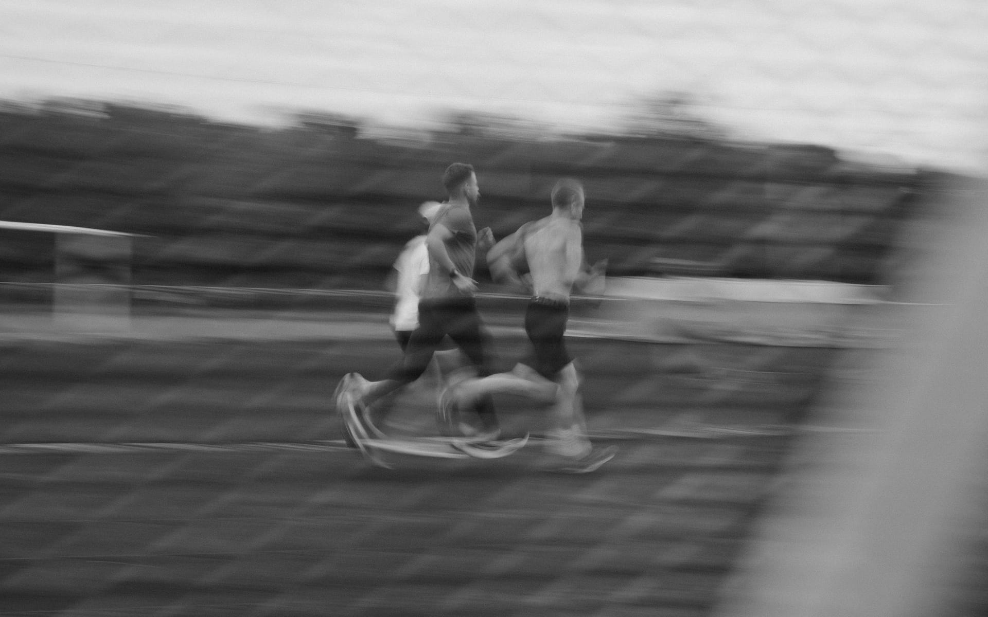 Three runners mid-stride on a track, the stands behind them streaked by motion blur.